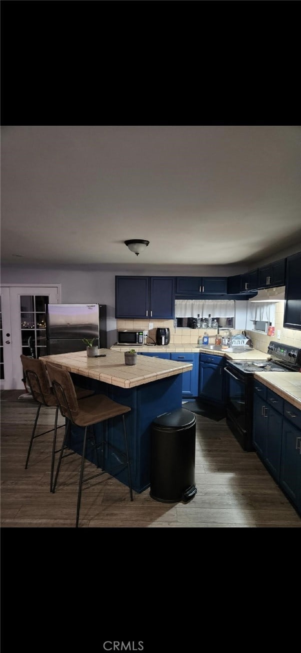 kitchen featuring dark wood-type flooring, a breakfast bar area, appliances with stainless steel finishes, backsplash, and blue cabinets