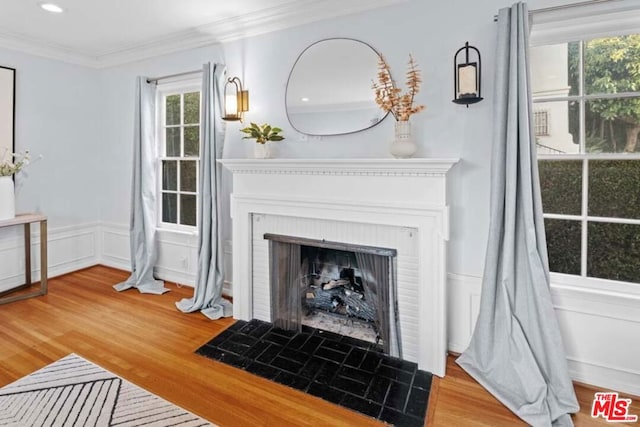 living room with a brick fireplace, wood-type flooring, and ornamental molding