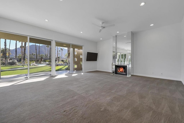 unfurnished living room featuring a mountain view, carpet flooring, a wealth of natural light, and ceiling fan