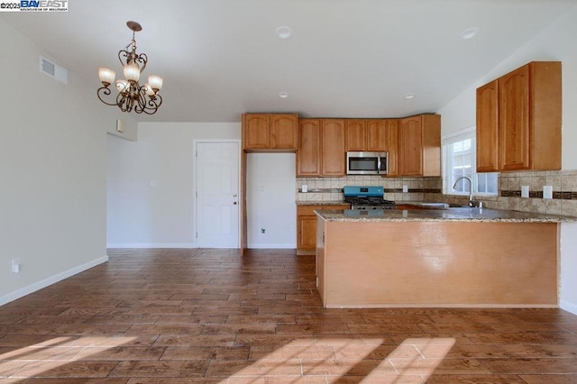 kitchen featuring an inviting chandelier, backsplash, hanging light fixtures, range, and sink