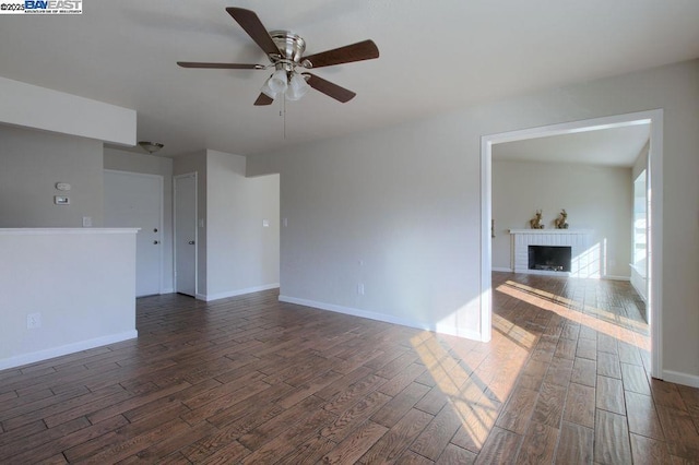 unfurnished living room with ceiling fan, a brick fireplace, and dark hardwood / wood-style flooring