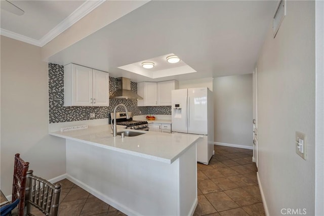 kitchen with white fridge with ice dispenser, white cabinets, gas stove, wall chimney range hood, and kitchen peninsula