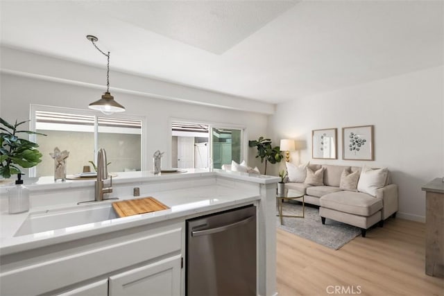 kitchen with stainless steel dishwasher, sink, decorative light fixtures, light wood-type flooring, and white cabinets