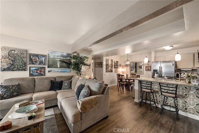 living room featuring dark wood finished floors, an inviting chandelier, a textured ceiling, beamed ceiling, and baseboards