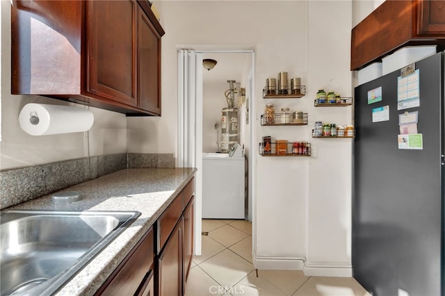 kitchen with washer / clothes dryer, sink, gas water heater, light tile patterned floors, and stainless steel fridge