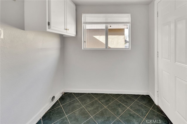 clothes washing area with cabinets and dark tile patterned floors