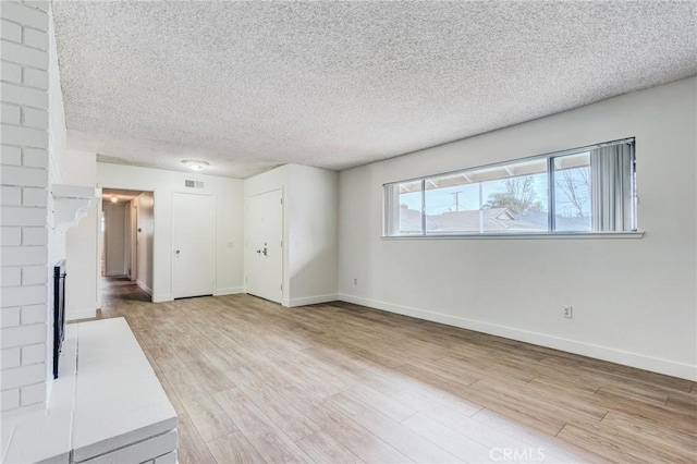 unfurnished living room with a textured ceiling, a brick fireplace, and light wood-type flooring