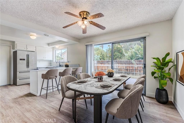 dining room with ceiling fan, sink, light hardwood / wood-style floors, and a textured ceiling