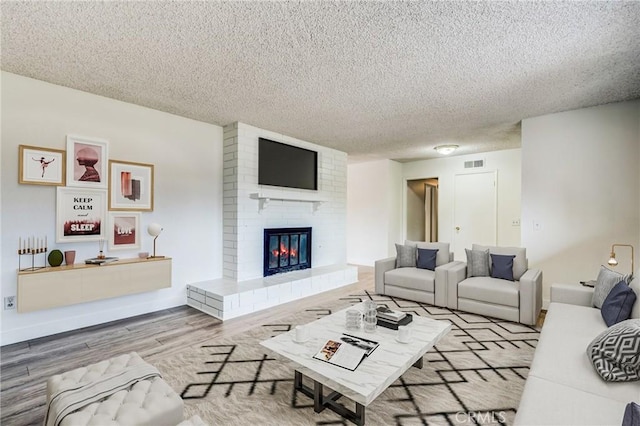 living room with a brick fireplace, a textured ceiling, and light wood-type flooring