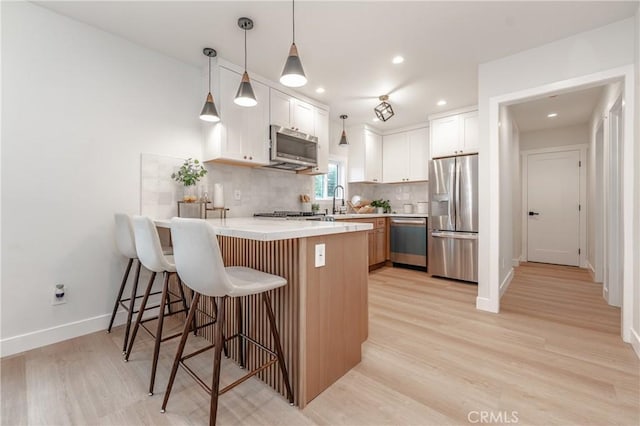 kitchen with light hardwood / wood-style flooring, appliances with stainless steel finishes, white cabinetry, decorative backsplash, and kitchen peninsula