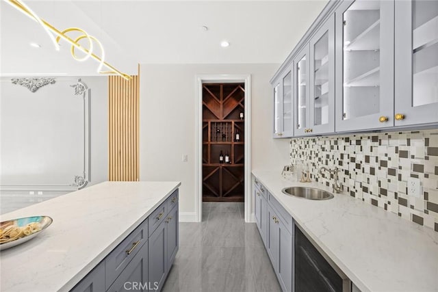 kitchen with light stone countertops, decorative light fixtures, tasteful backsplash, sink, and gray cabinets