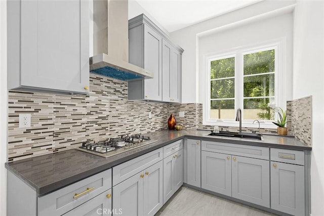 kitchen featuring gray cabinets, decorative backsplash, stainless steel gas cooktop, wall chimney range hood, and sink