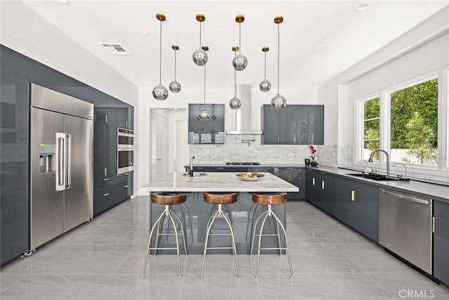 kitchen featuring appliances with stainless steel finishes, decorative light fixtures, wall chimney range hood, a kitchen island, and sink