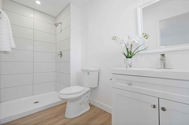 bathroom featuring toilet, a tile shower, hardwood / wood-style flooring, and vanity