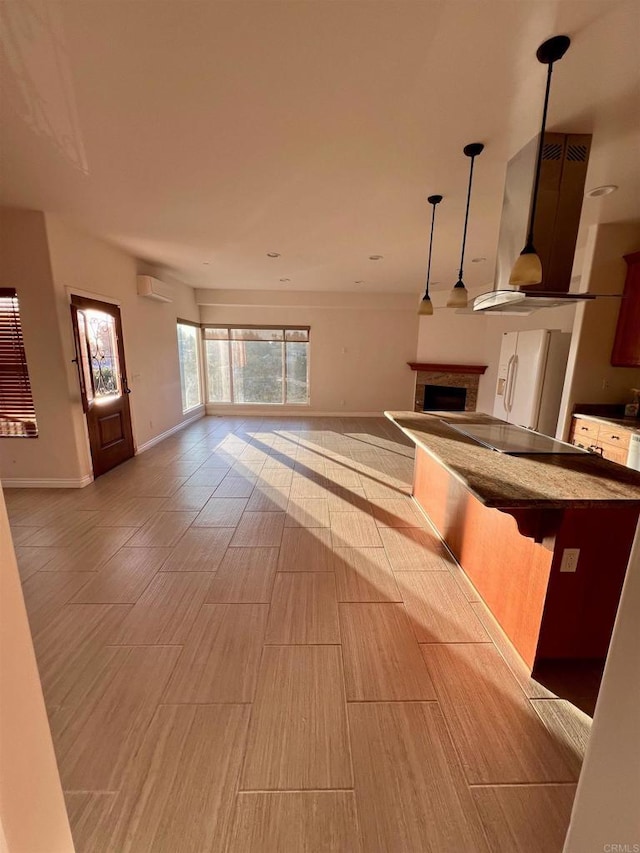 kitchen featuring black electric cooktop, white fridge with ice dispenser, hanging light fixtures, wall chimney range hood, and an AC wall unit