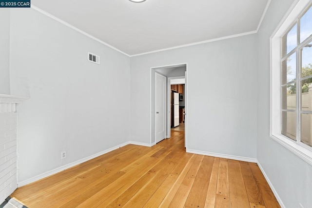 spare room with a brick fireplace, crown molding, light hardwood / wood-style floors, and plenty of natural light