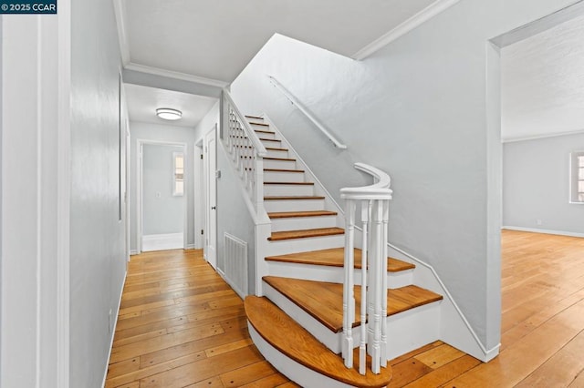 stairway with wood-type flooring and ornamental molding