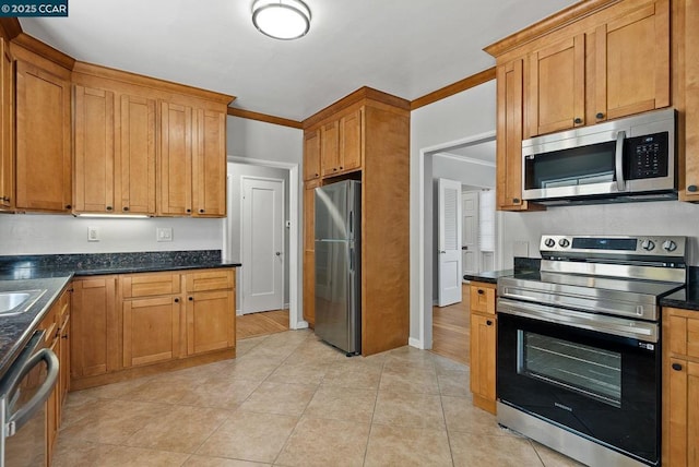 kitchen with dark stone counters, light tile patterned flooring, stainless steel appliances, and ornamental molding