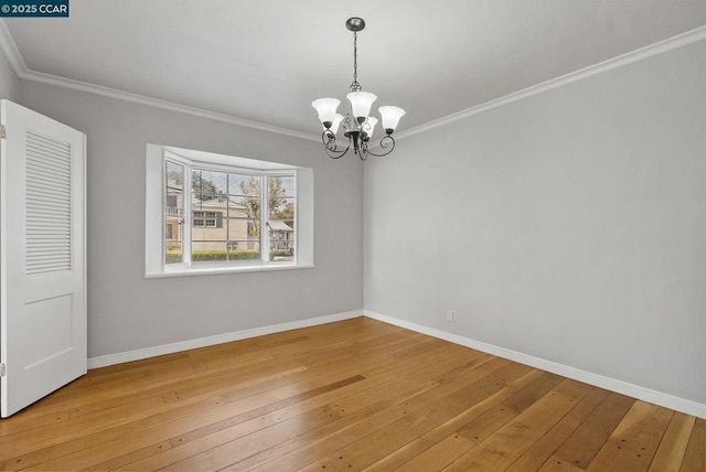 spare room with a notable chandelier, ornamental molding, and hardwood / wood-style floors