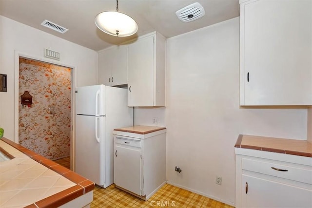 kitchen featuring decorative light fixtures, white fridge, white cabinetry, and tile counters