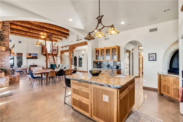 kitchen featuring beam ceiling, decorative light fixtures, ceiling fan, and a center island with sink