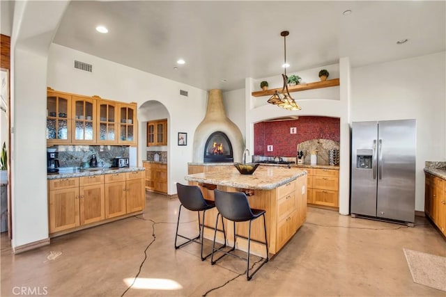 kitchen with stainless steel refrigerator with ice dispenser, backsplash, a fireplace, a kitchen island, and pendant lighting