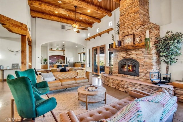 living room featuring a towering ceiling, a fireplace, ceiling fan, wooden ceiling, and beam ceiling