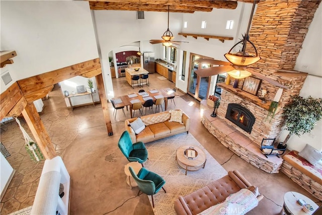 living room featuring ceiling fan, beamed ceiling, a stone fireplace, and a towering ceiling