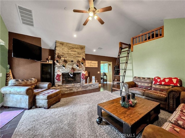 living room featuring ceiling fan, a stone fireplace, and vaulted ceiling