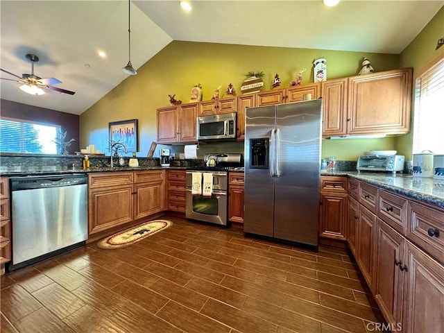 kitchen featuring decorative light fixtures, ceiling fan, lofted ceiling, stainless steel appliances, and dark stone counters