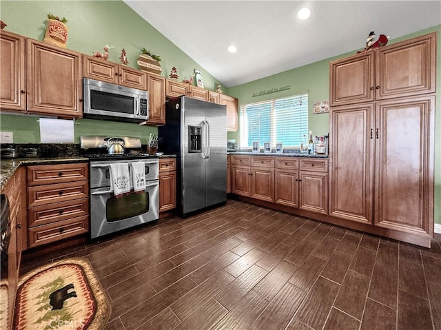 kitchen featuring vaulted ceiling, stainless steel appliances, and dark stone countertops