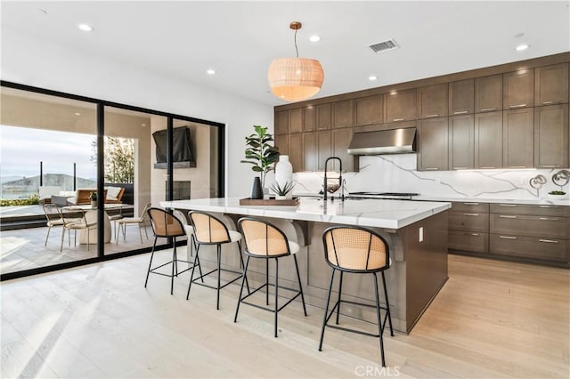 kitchen featuring tasteful backsplash, light hardwood / wood-style floors, an island with sink, a kitchen bar, and decorative light fixtures