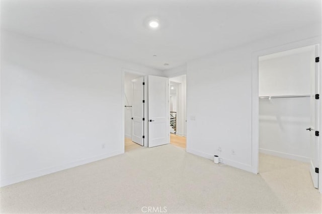 unfurnished bedroom featuring a spacious closet, light colored carpet, and a closet