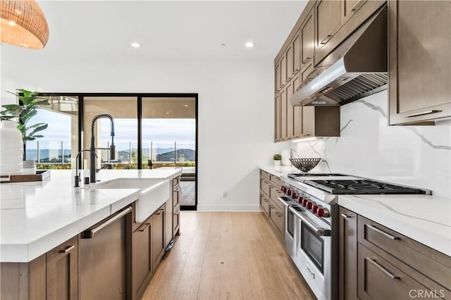 kitchen featuring sink, light wood-type flooring, light stone countertops, and appliances with stainless steel finishes