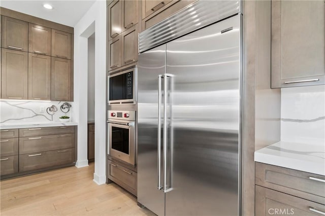 kitchen with built in appliances, light stone counters, and light wood-type flooring