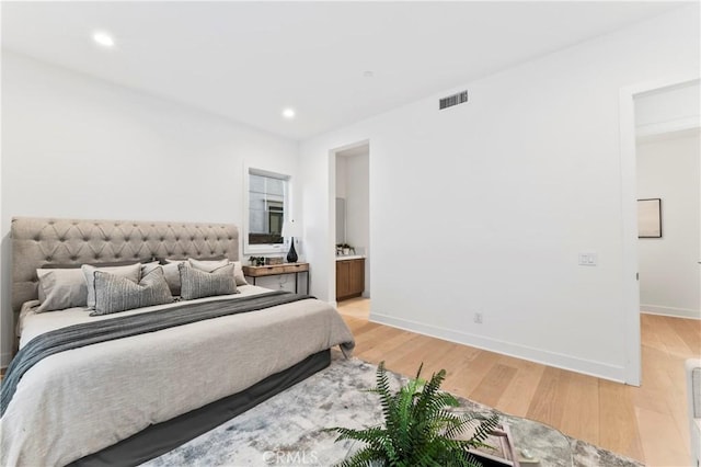 bedroom with connected bathroom and light hardwood / wood-style floors