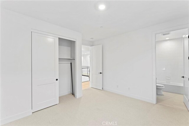 unfurnished bedroom with light carpet, ensuite bath, and a closet