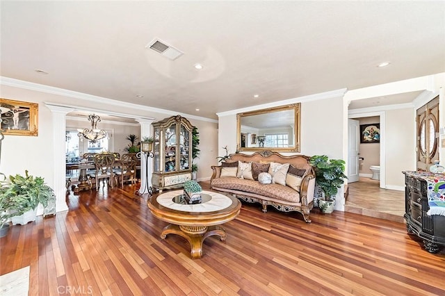 living room with wood-type flooring, crown molding, a chandelier, and decorative columns