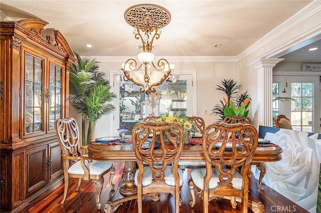 dining space with decorative columns, dark wood-type flooring, crown molding, and a notable chandelier