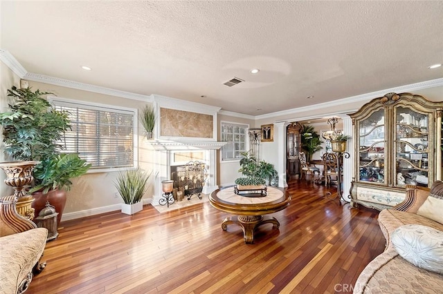 living room with hardwood / wood-style flooring, decorative columns, a tiled fireplace, a textured ceiling, and crown molding