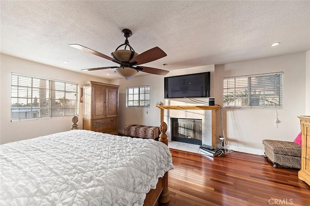 bedroom featuring ceiling fan, hardwood / wood-style floors, a tiled fireplace, and multiple windows