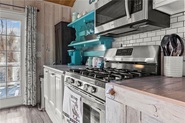 kitchen with stainless steel appliances, wooden walls, wood-type flooring, and backsplash