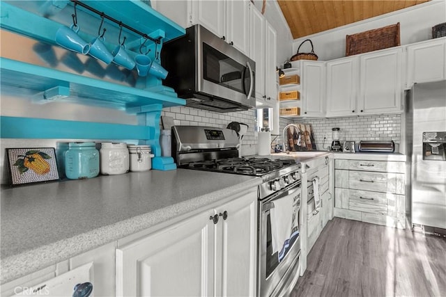 kitchen with vaulted ceiling, appliances with stainless steel finishes, sink, white cabinets, and backsplash