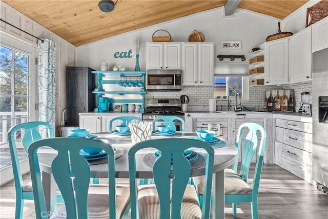 kitchen with stainless steel appliances, white cabinets, and lofted ceiling with beams