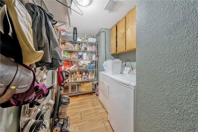 laundry room featuring washer and clothes dryer, a textured ceiling, light hardwood / wood-style floors, and cabinets