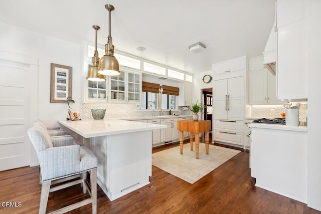 kitchen with white cabinets, decorative light fixtures, dark wood-type flooring, kitchen peninsula, and a breakfast bar area