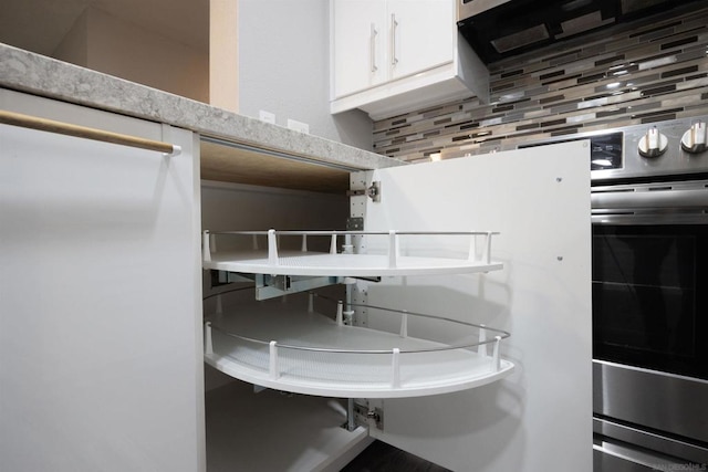 interior space with light stone countertops, white cabinets, backsplash, and oven