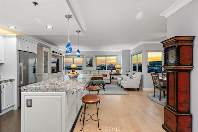 kitchen with a kitchen bar, white cabinetry, stainless steel refrigerator with ice dispenser, decorative light fixtures, and ornamental molding