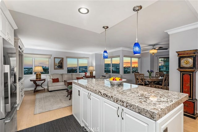 kitchen featuring white cabinetry, stainless steel refrigerator, a kitchen island, decorative light fixtures, and ornamental molding