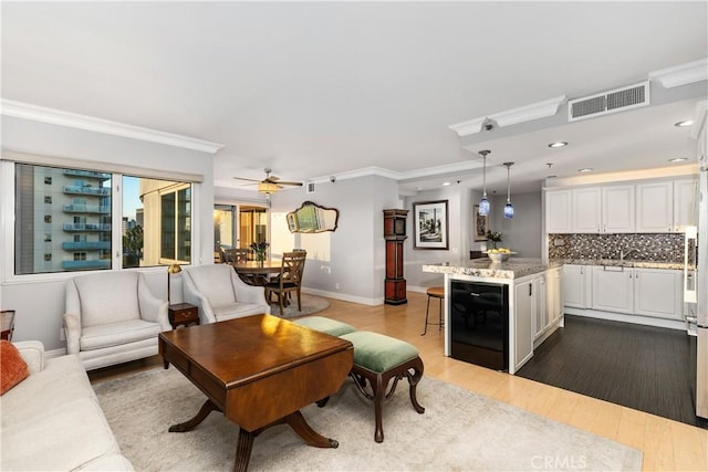 living room with light hardwood / wood-style floors, sink, ornamental molding, ceiling fan, and wine cooler